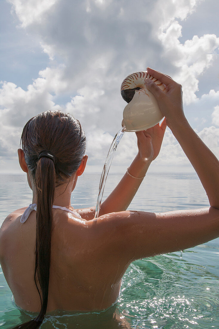 Frau im Meer, die Wasser aus einer Nautilus-Muschel gießt