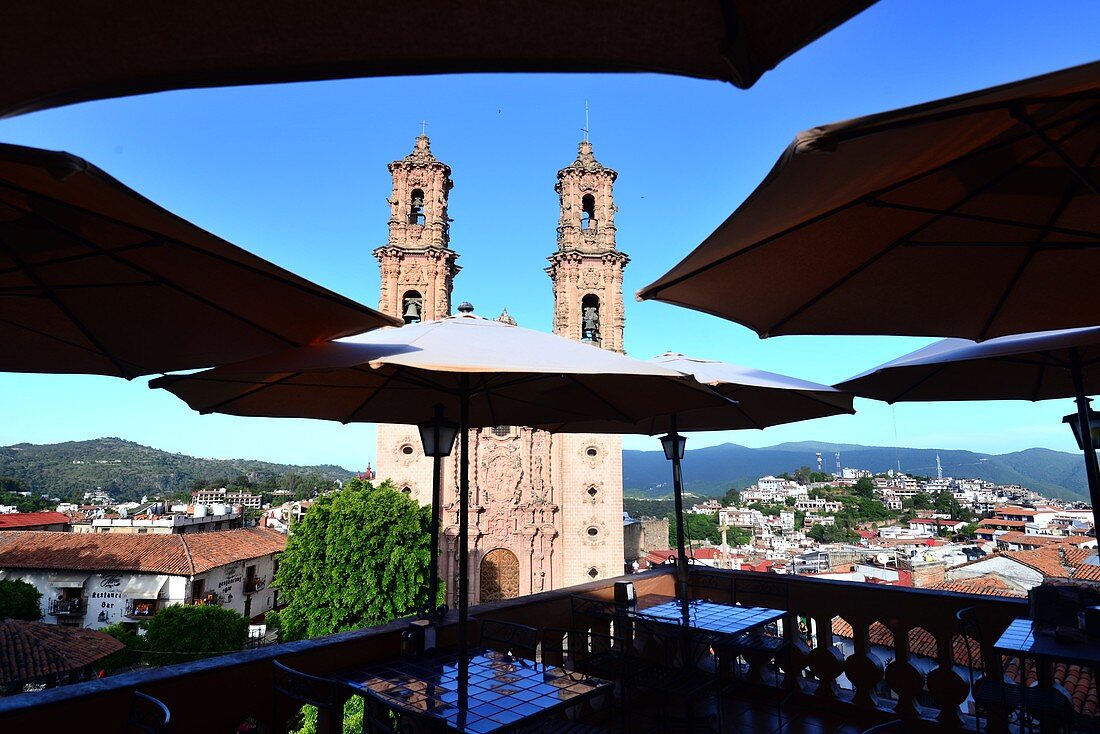 Blick vom Dach eines Restaurants mit Schirmen auf die Igleisia de Santa Prisca in der Altstadt von Taxco, Mexiko