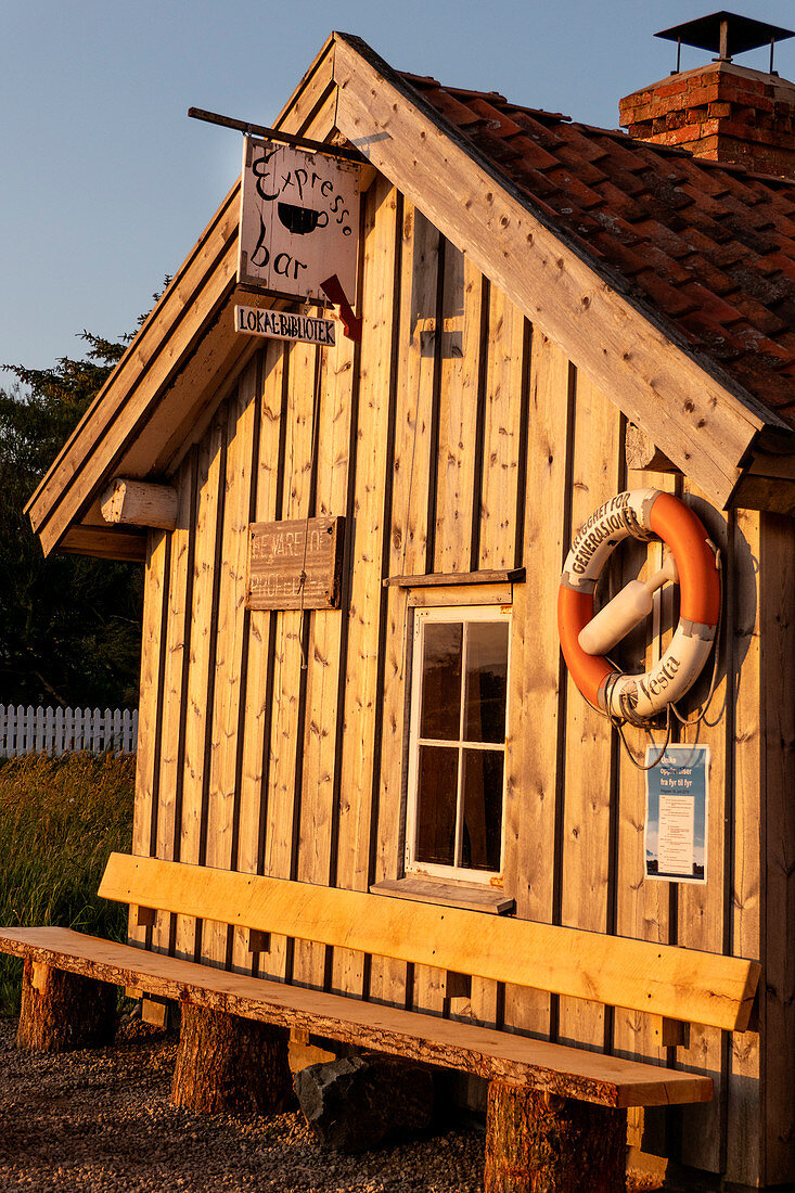 Coffee bar wooden hut stands in the sunset on the coast in Penne, Norway. A lifebuoy hangs ready. A wooden bench to rest stands in front of the wooden house.