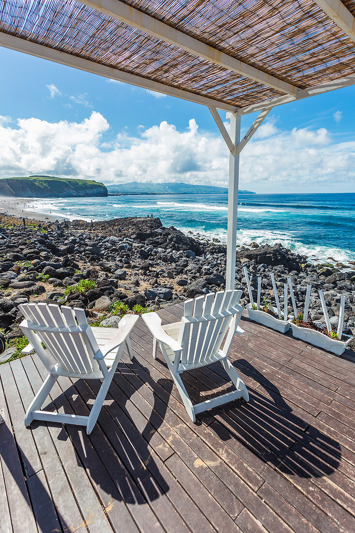 Two wooden lounge chairs sitting on the deck overlooking the ocean in Azores Islands, Sao Miguel, Portugal