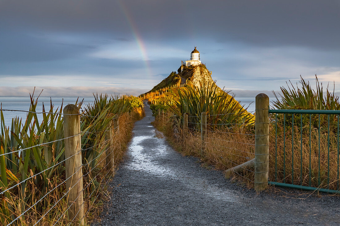 Regenbogen am Nugget Point Leuchtturm nach dem Sturm. Ahuriri-Ebene, Clutha-Bezirk, Otago-Region, Südinsel, Neuseeland