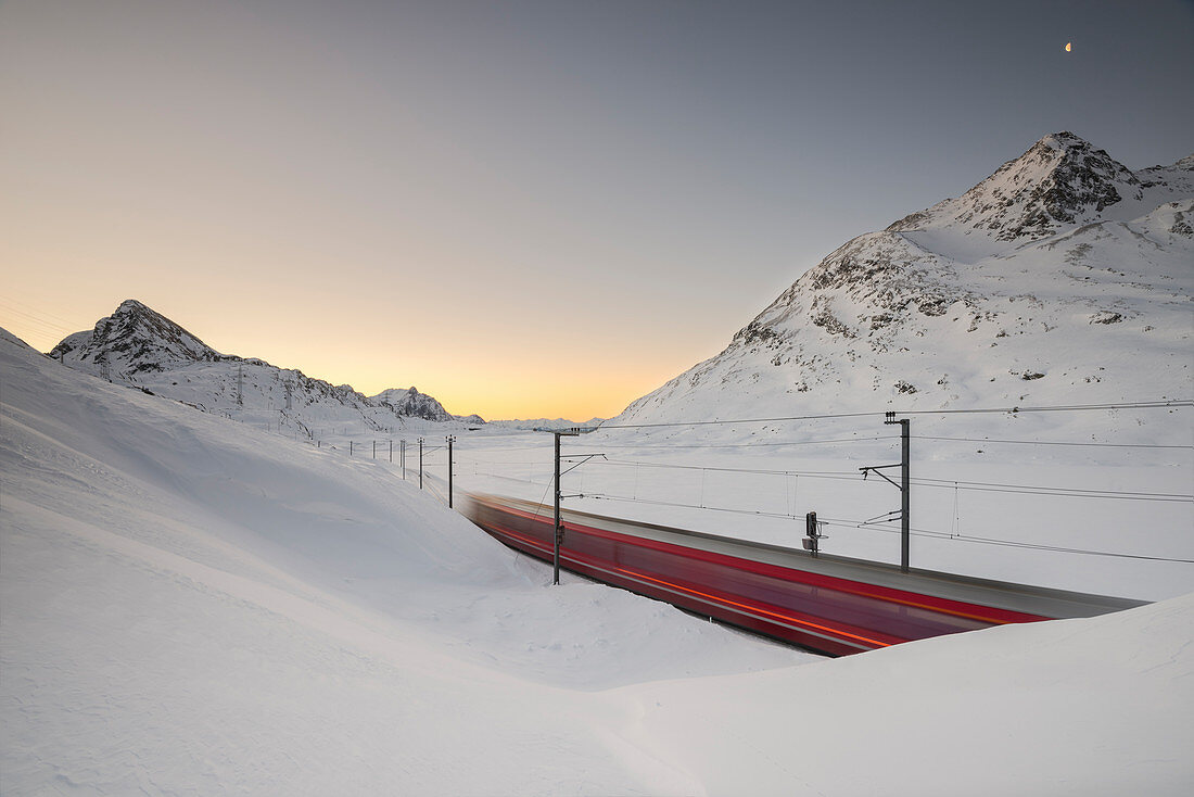 Der Bernina-Expresszug fährt am schneebedeckten Bianco-See entlang Berninapass mit einigen Blasen, Kanton Graubünden, Engadin, Schweiz, Europa