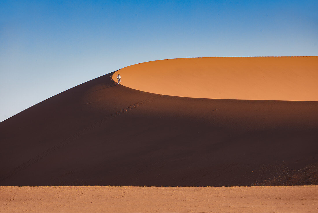 Ein Mann lüft auf einer Düne in der Wüste Namib, Namib Naukluft Park, Namibia