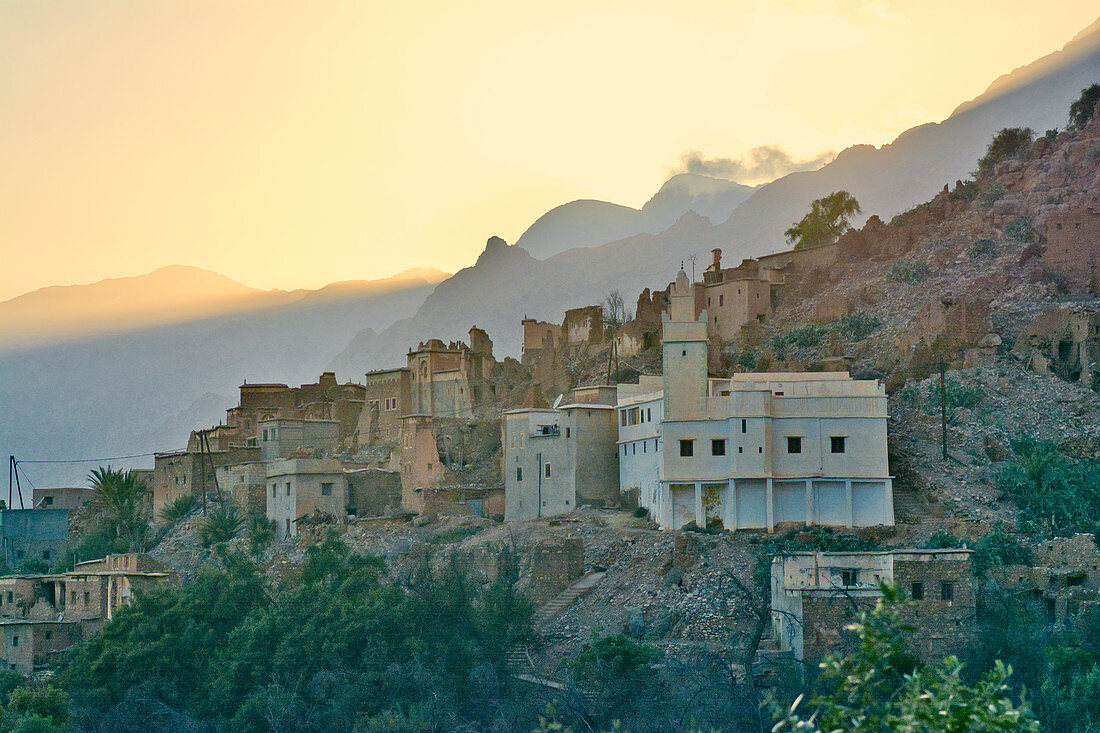 Das Dorf Oumesnat kurz nach Sonnenuntergang am Fuss steiler Berge, Tal der Ammeln im Antiatlas, Marokko