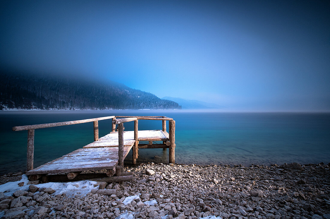 Lichtkegel auf schneebedeckten Holzsteg, Walchensee bei Nebel im Winter, Bayern, Deutschland