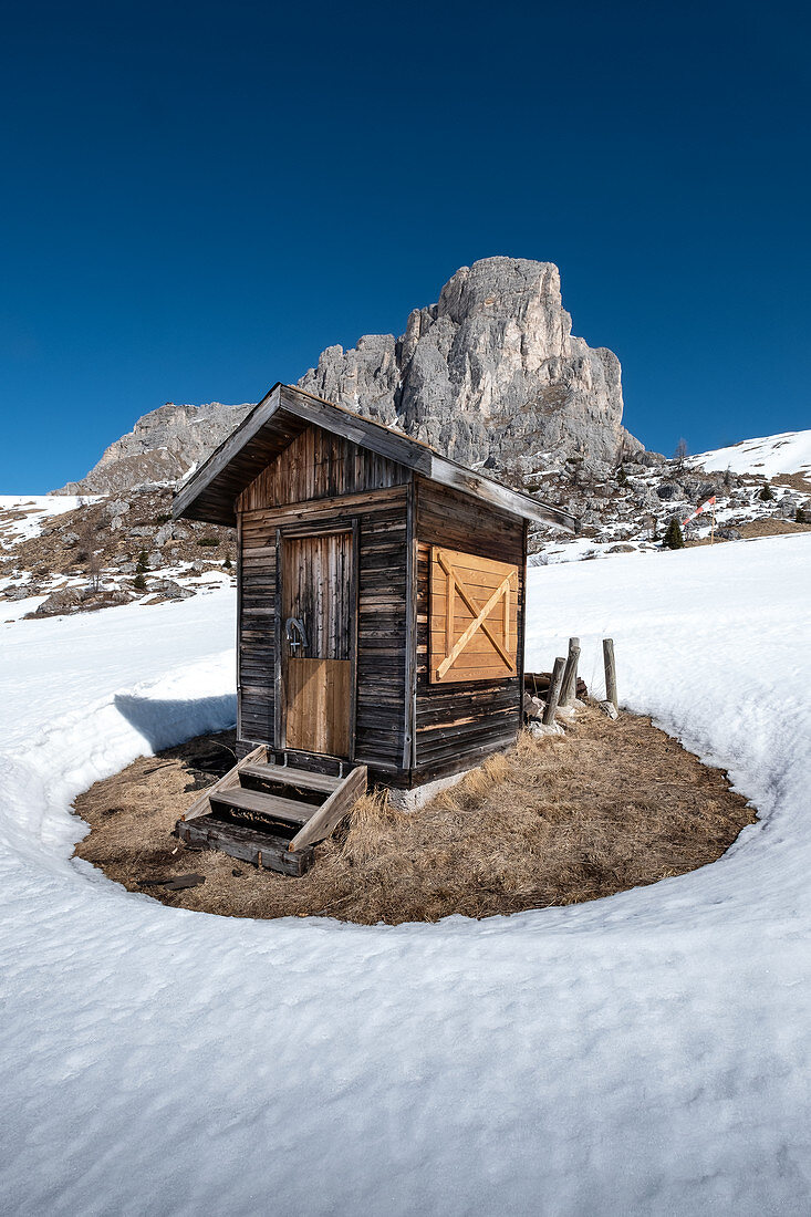 Wooden hut in the snow at Passo di Giau in winter. Transition to spring, vertical format, Dolomites, Cortina d'Ampezzo, Belluna, Italy
