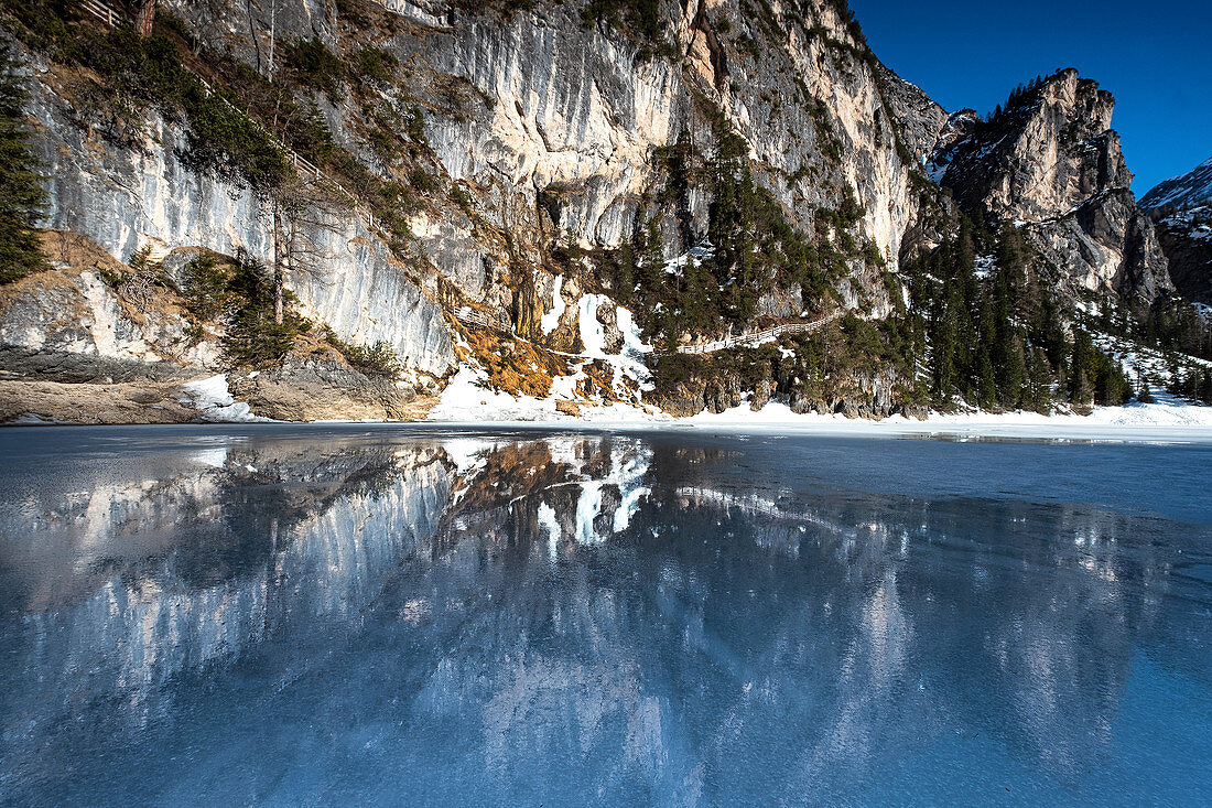 Reflection from frozen Lake Braies, in the background a walk along the mountain massif in winter, Dolomites, Lago di Braies, Braies, South Tyrol, Italy