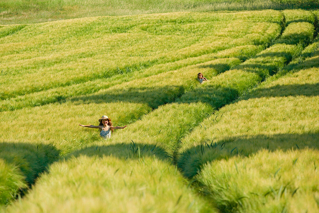 Carefree girls running in sunny, idyllic green rural wheat field