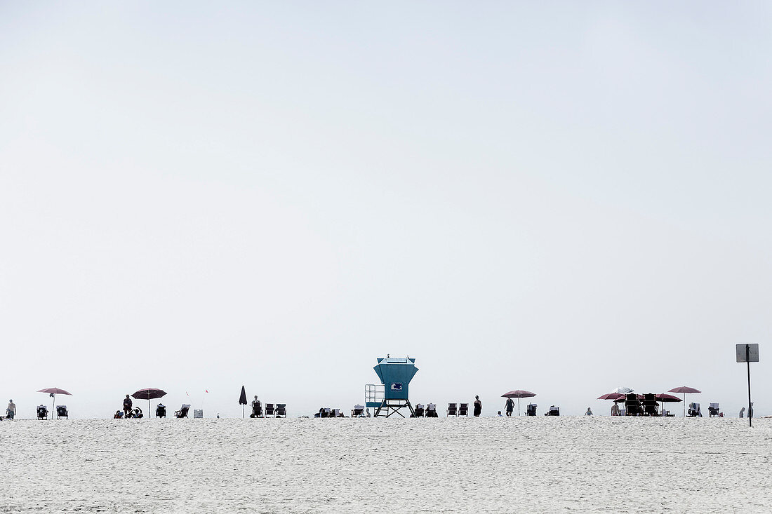 Lifeguard tower and people relaxing under umbrellas on sunny beach, San Diego, California, USA