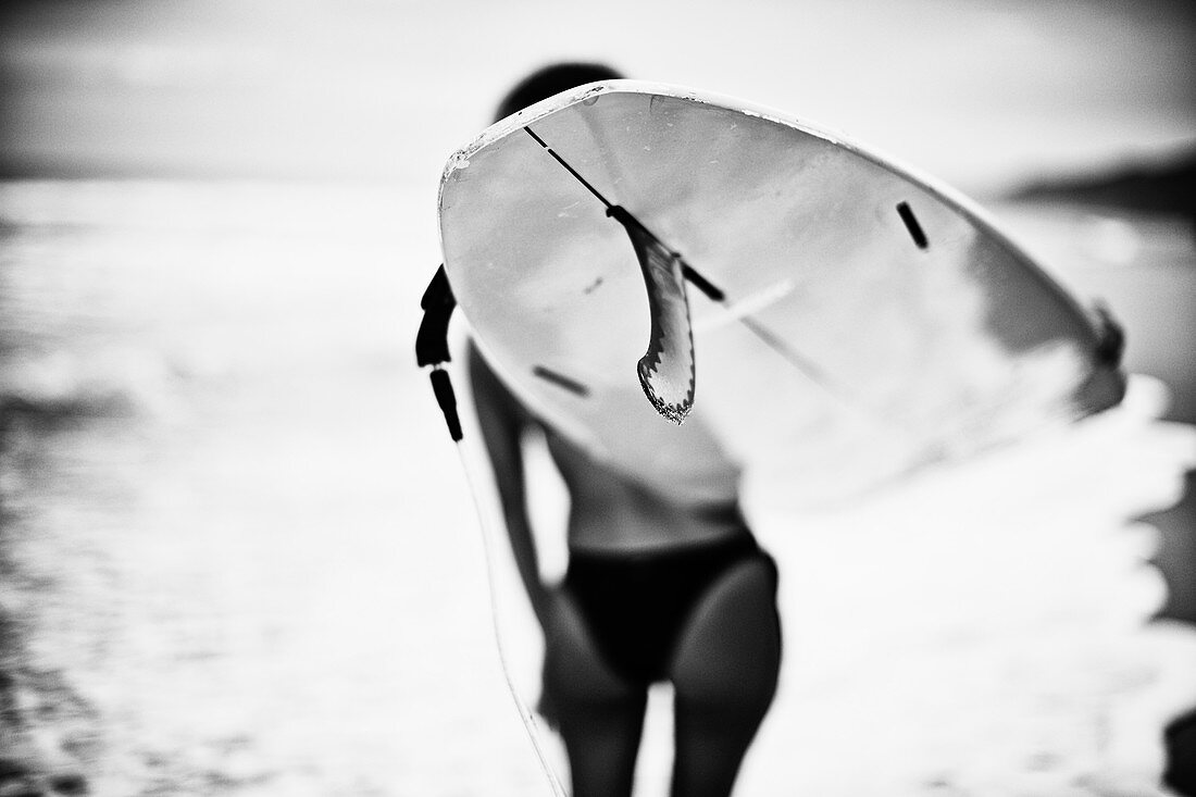 Frau trägt Surfbrett am Strand