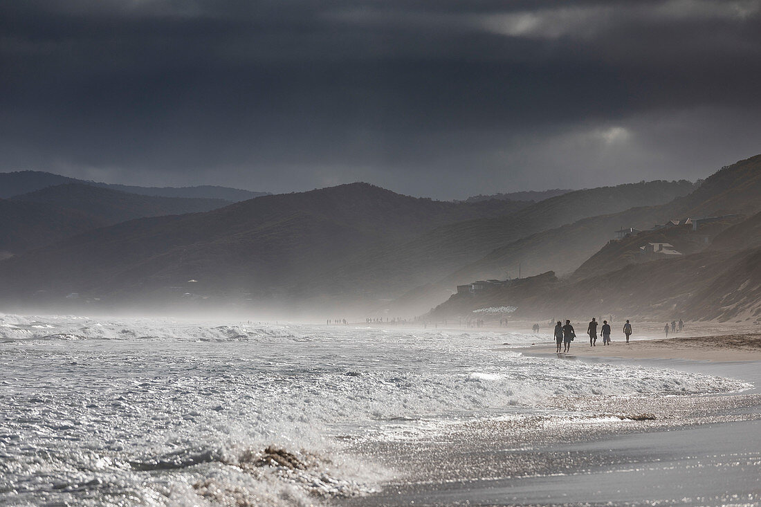 Ominous clouds over silhouetted people walking on ocean beach, Aireys Inlet, Victoria, Australia