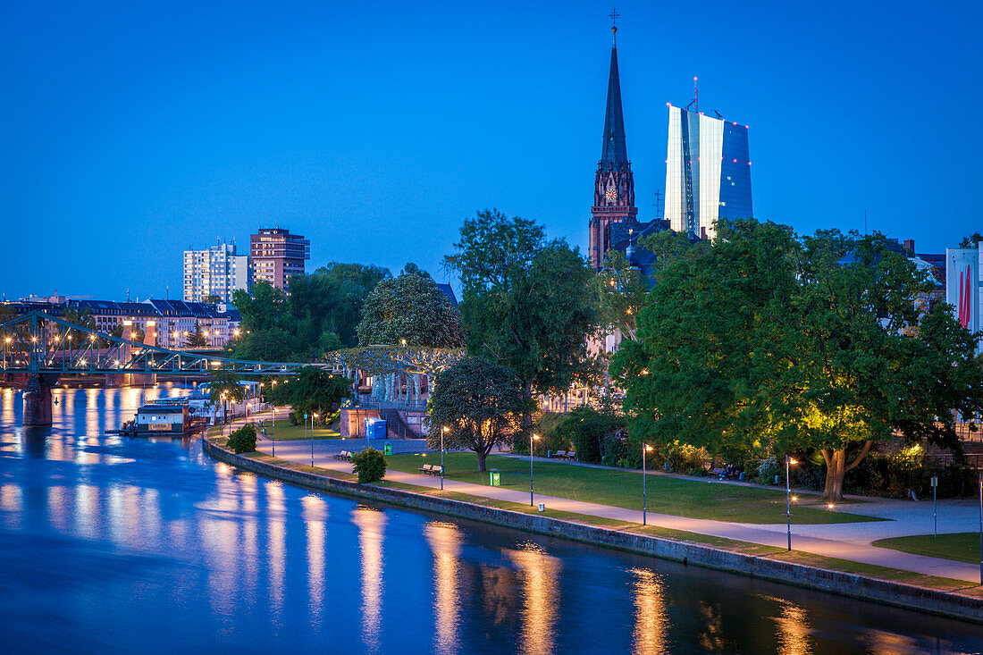 Blick über Fluss auf Kirchenturm und Büro-Hochhäuser bei Sonnenuntergang in Frankfurt, Deutschland