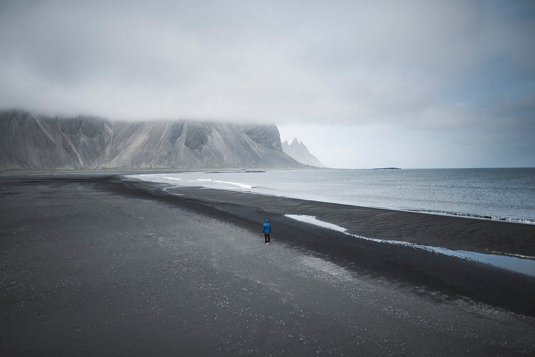 Mann am schwarzen Sandstrand in Kirkjubaejarklaustur, Island
