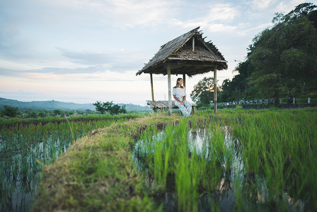 Woman sitting in hut by rice paddy in Bali, Indonesia