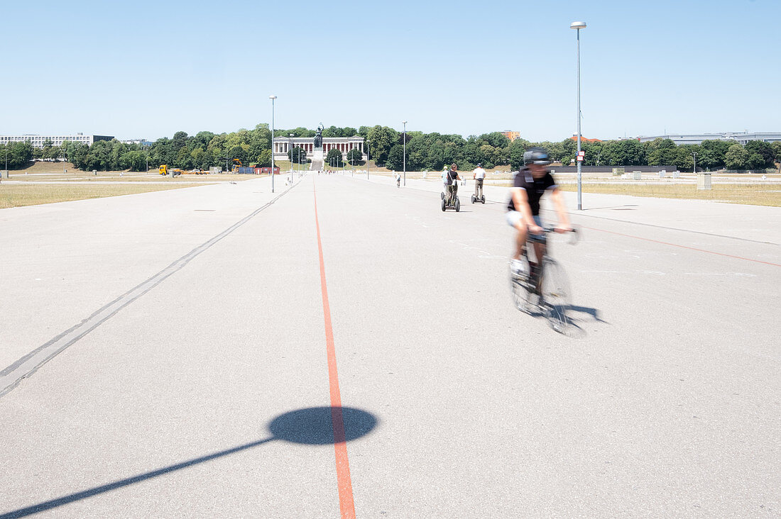 Bicycle rider on the Theresienwiese, in the background the Bavaria, Munich, Bavaria, Germany