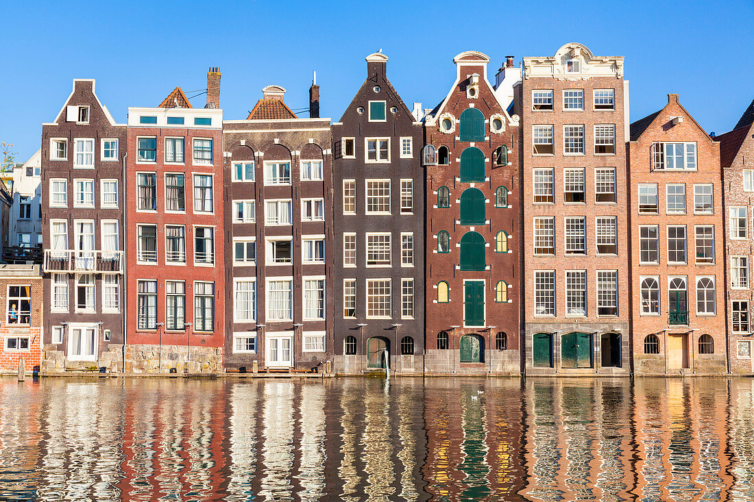 Niederländische Giebel in der Reihe von typischen Amsterdam-Häusern nachts mit Reflexionen im Damrak-Kanal, Amsterdam, Nordholland, die Niederlande, Europa