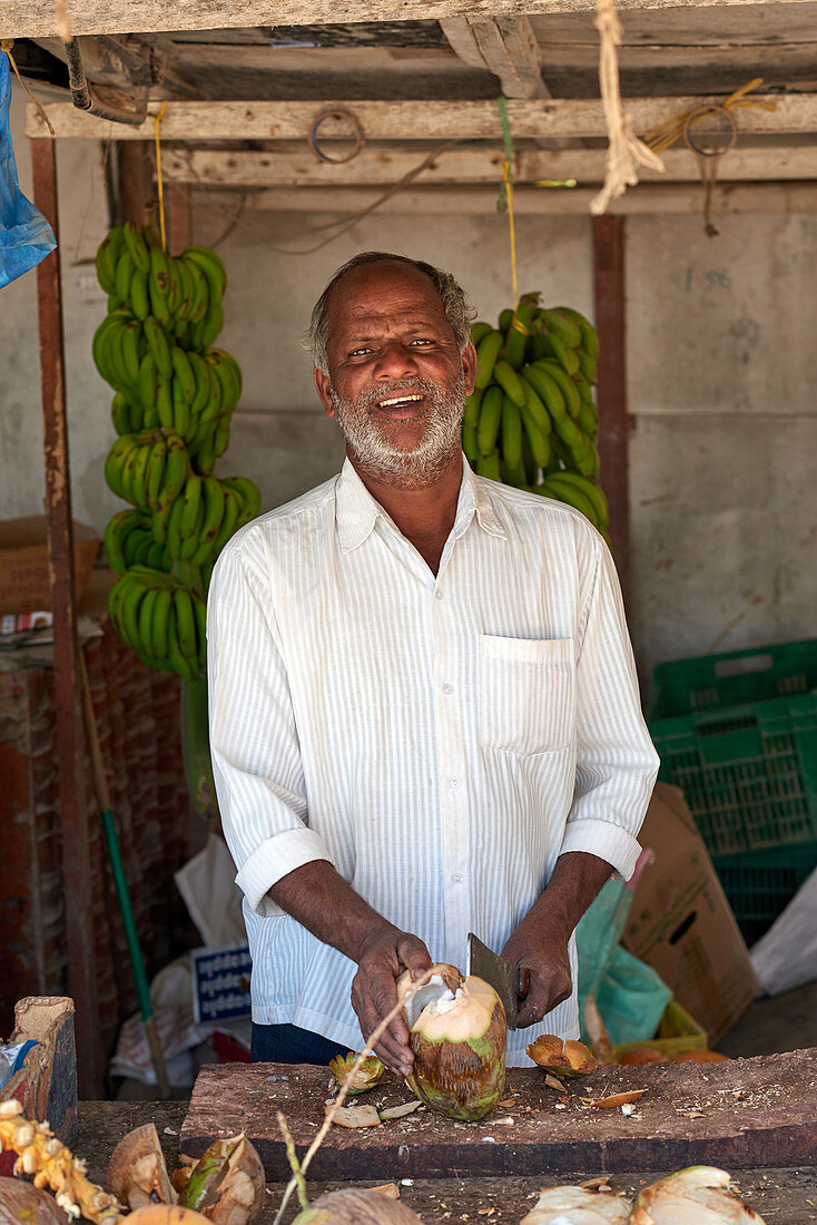 Fruchtverkäufer mit Kokosnuss an seinem Stand in Salala, Oman