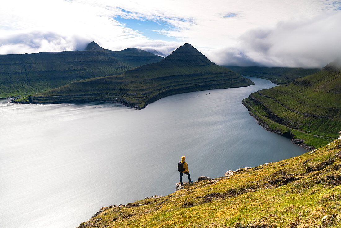 Hiker on rocks looks at the fjords, Funningur, Eysturoy island, Faroe Islands, Denmark, Europe