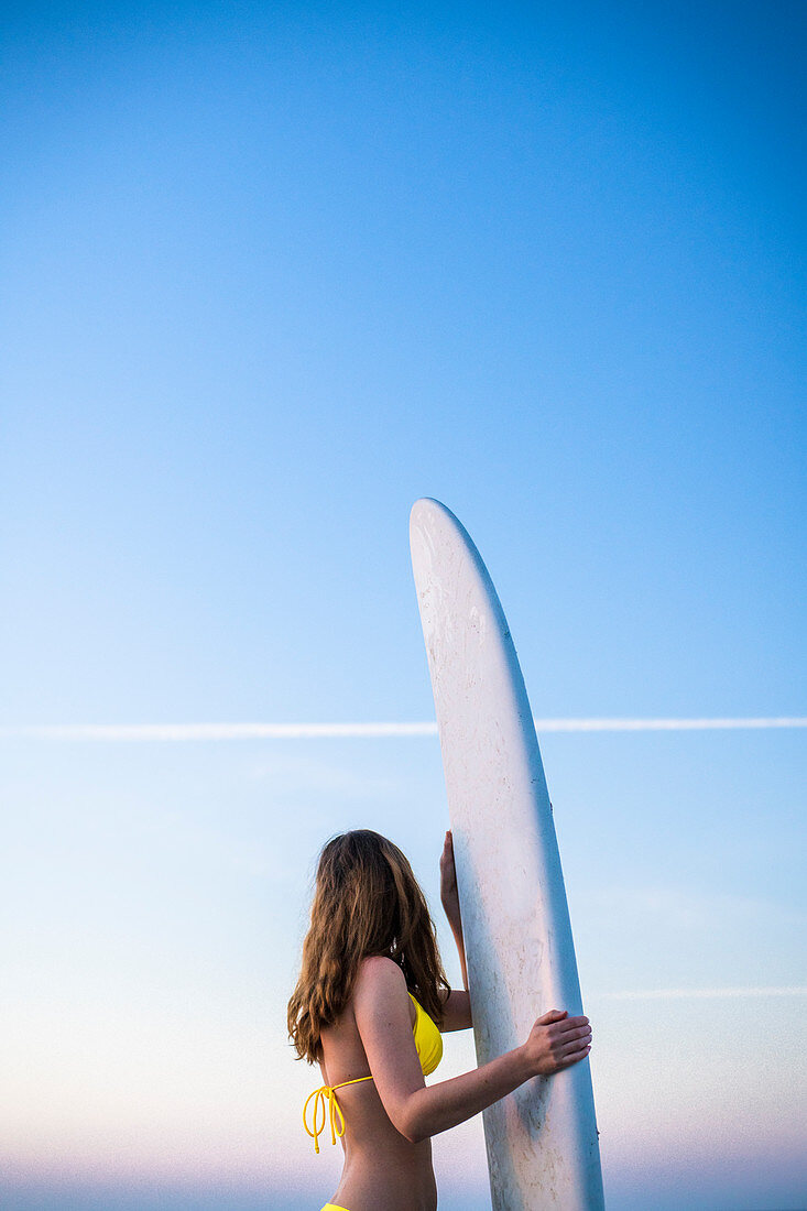 Side view shot of woman in yellow bikini standing with surfboard