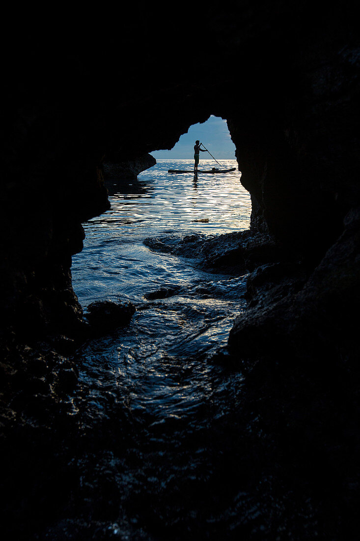View from cave of silhouette of man paddleboarding in sea, Misool, Raja Ampat, Indonesia