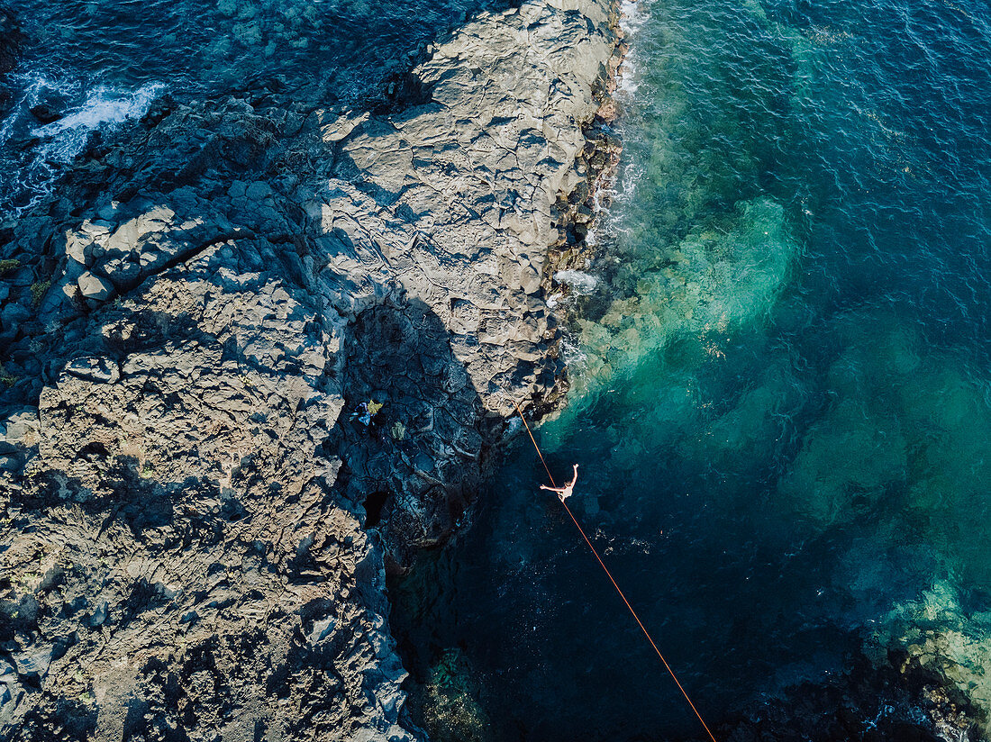 Aerial view of young shirtless man balancing across tightrope over coastal water,†Tenerife, Canary Islands, Spain