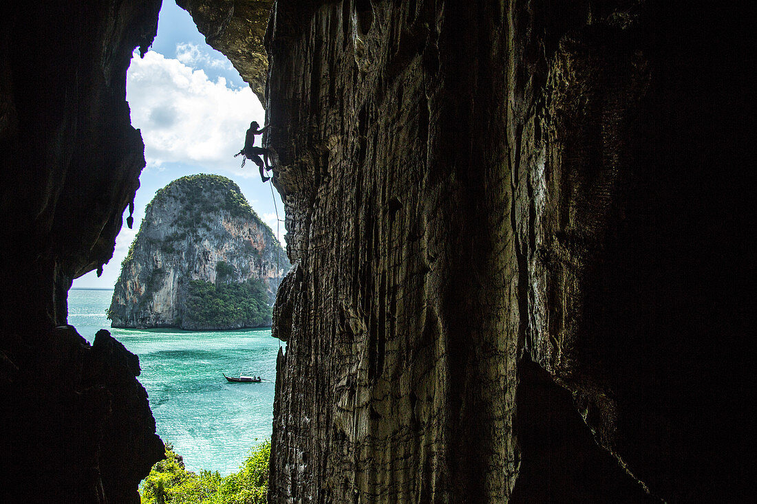 Side view silhouette of man rock climbing in beautiful natural scenery on edge of cave, Phra Nang Beach, Krabi, Thailand