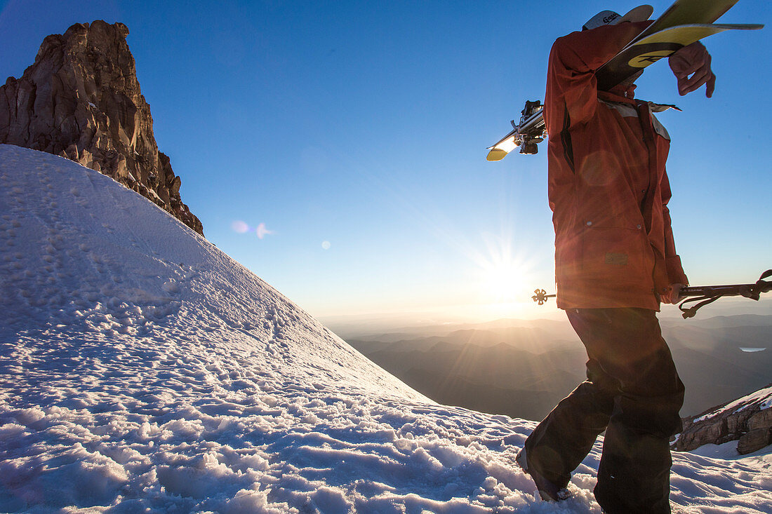 Skifahrer mit Skiern auf dem verschneiten Berg mit Sonnenuntergang im Hintergrund, Mount Hood, Oregon, USA