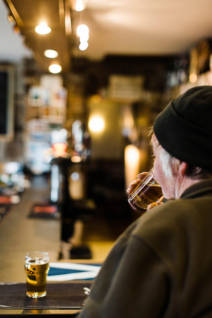 Rear view of older man enjoying glass of beer at pub, Scotland, UK