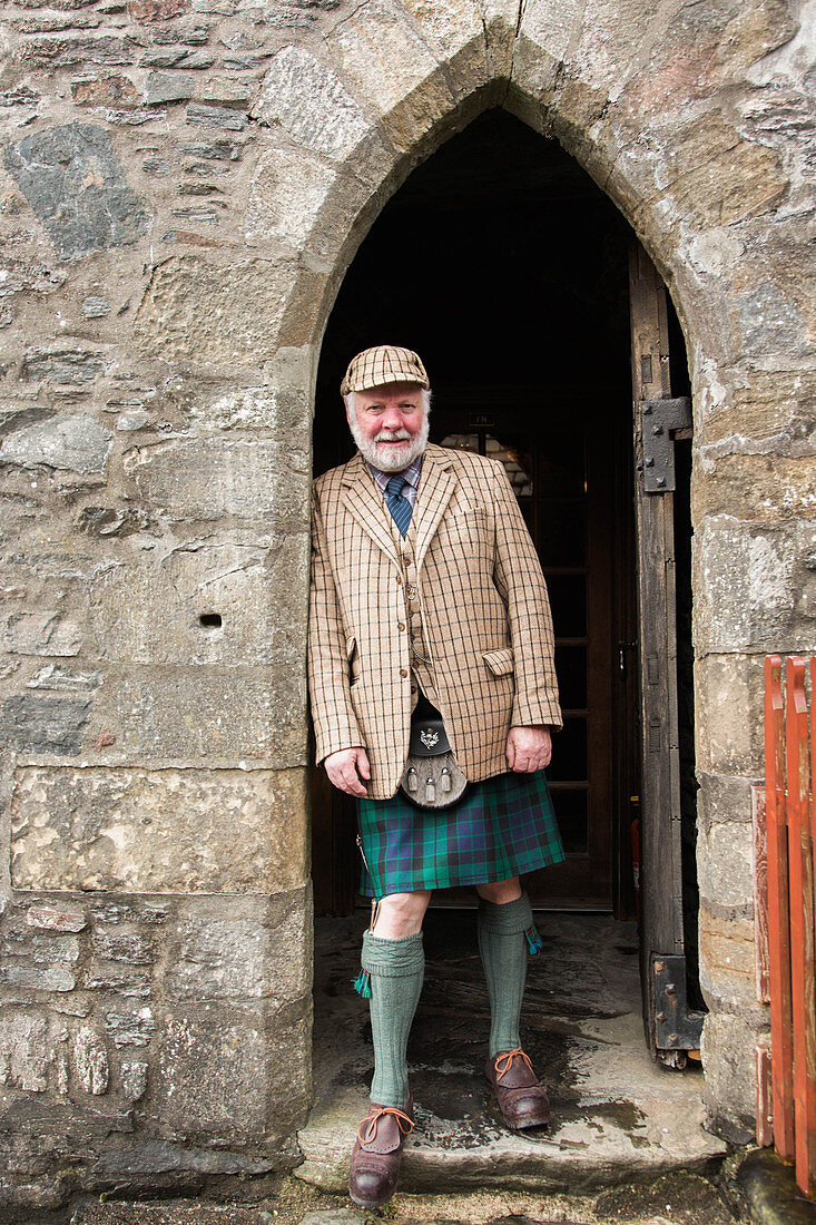 Portrait of mature man wearing traditional kilt leaning on archway of Eilean Donan Castle, Scotland, UK