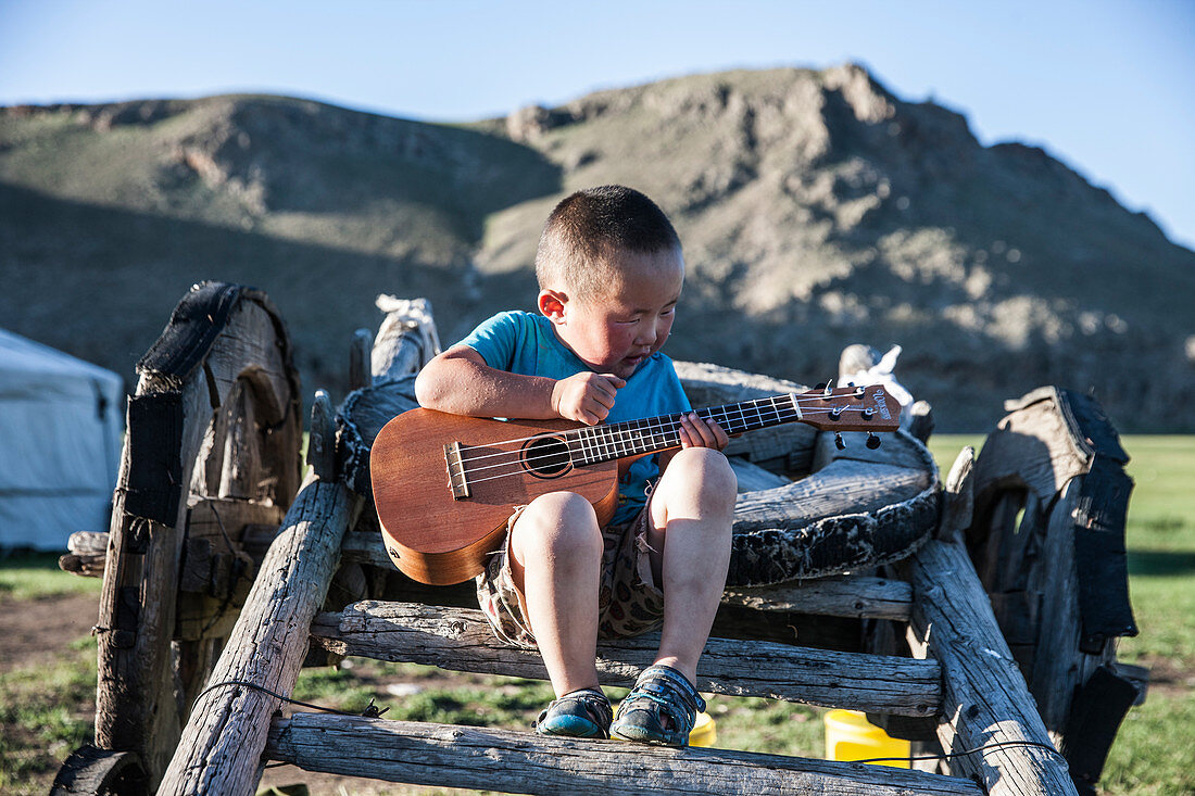 Mongolischer Junge auf Yakkarren sitzend spielt Gitarre, Bunkhan, Bulgan, Mongolei