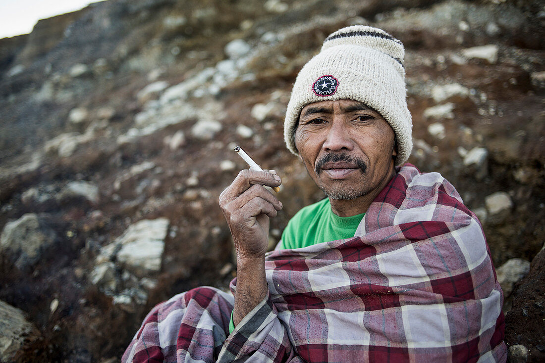 Porträt eines Schwefelbergarbeiters beim Zigarettenrauchen am Vulkan Kawah Ijen in Java, Indonesien
