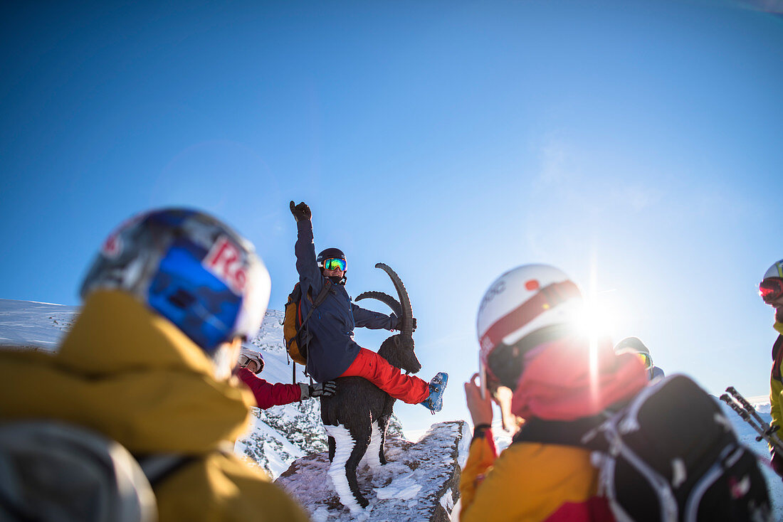 Professional skiers wearing skiwear, one sitting on ibex statue, Monterosa Ski mountain resort in Gressoney, Aosta, Italy