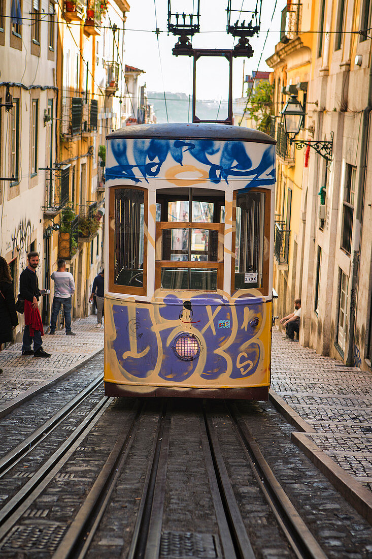 Painted tram waiting on rails across steep city street, Lisbon, Portugal