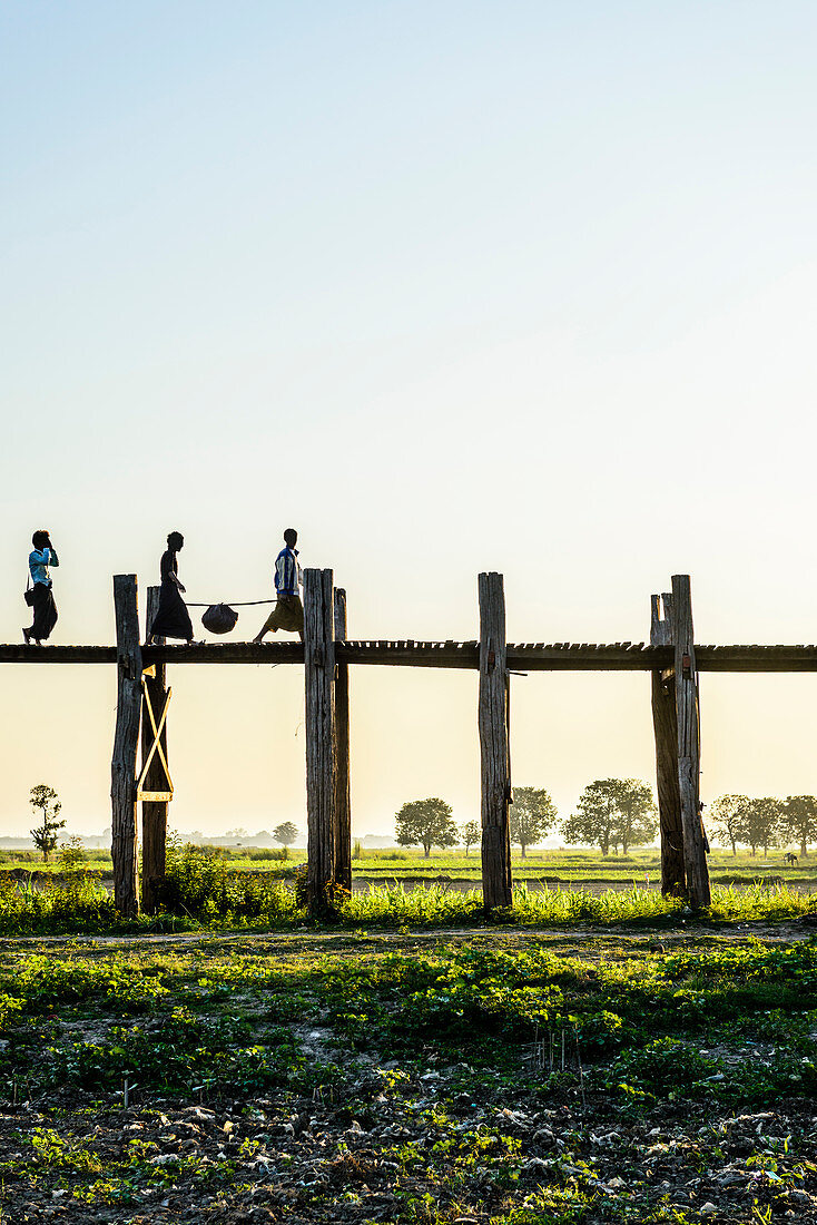 Menschen wandern auf erhöhten Holzstegen in ländlicher Landschaft, Myanmar, Burma