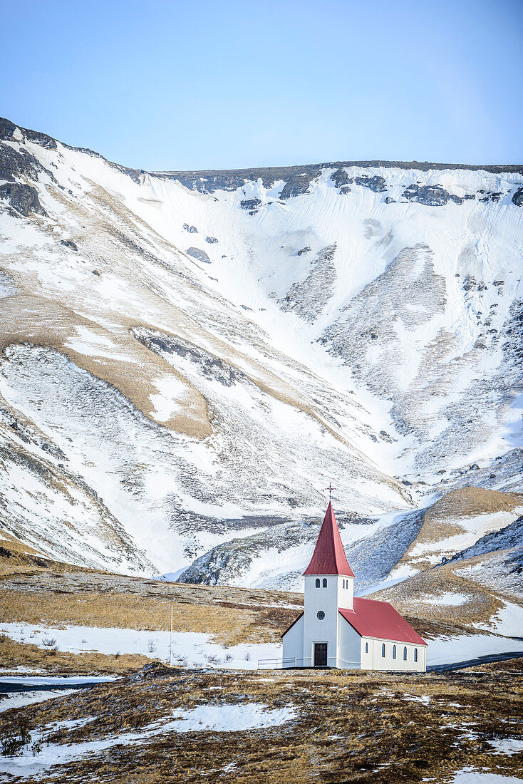 Kirche unter verschneiten Bergen in ländlicher Landschaft, Vik, Island
