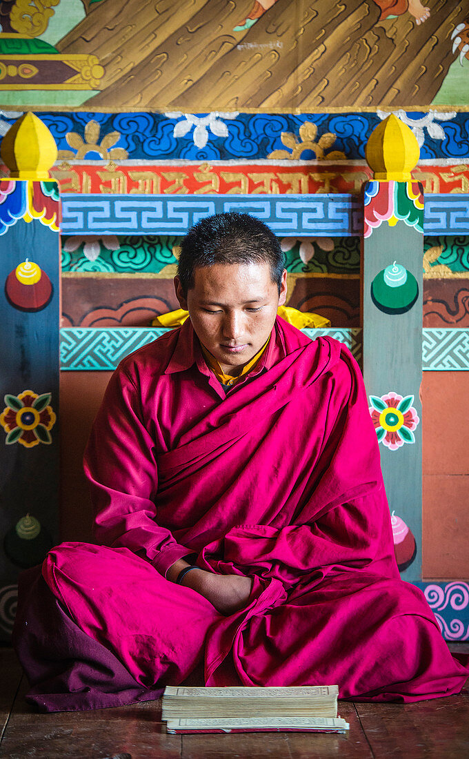 Asiatischer Mönch beim Lesen auf dem Tempelboden, Bhutan, Königreich Bhutan