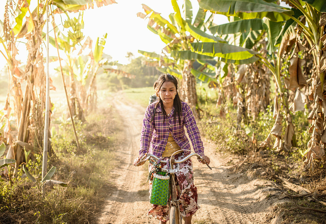 Asian woman riding bicycle on rural road, Myanmar