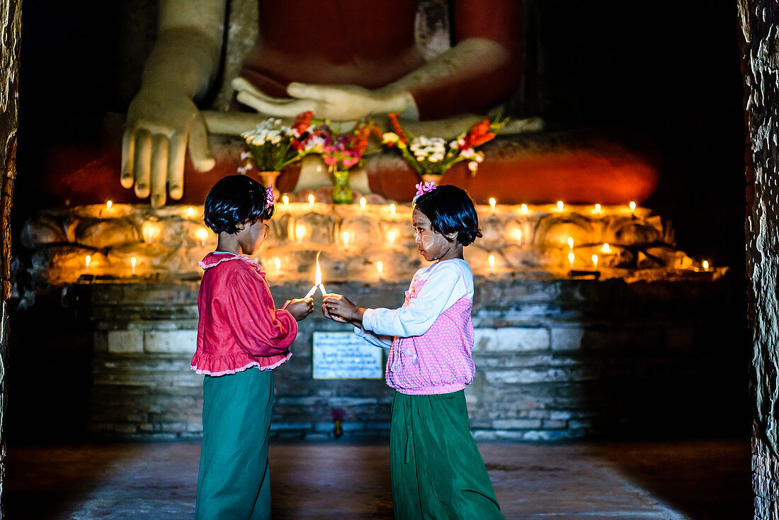 Asian girls lighting candles in Buddhist temple, Myanmar