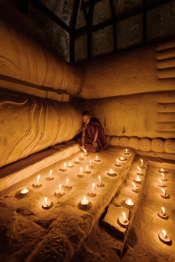 Asiatischer Mönch zündet Kerzen im Tempel an, Myanmar