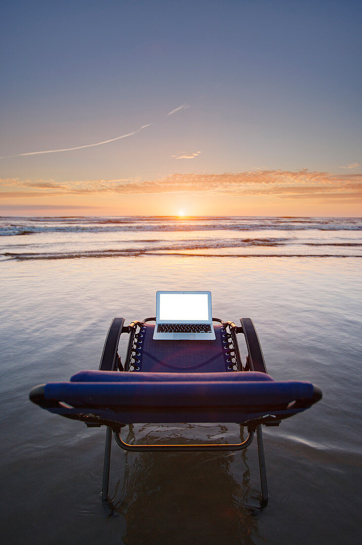 Laptop auf Liegestuhl mit Blick auf den Sonnenuntergang am Strand