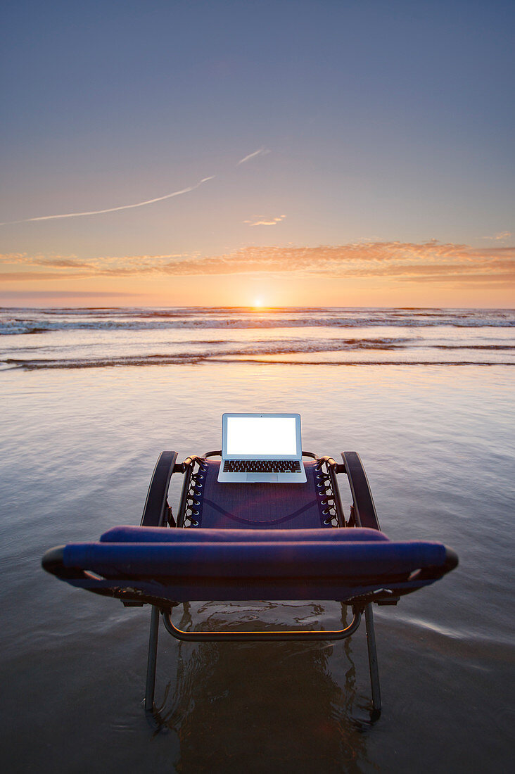Laptop on deck chair overlooking sunset on beach