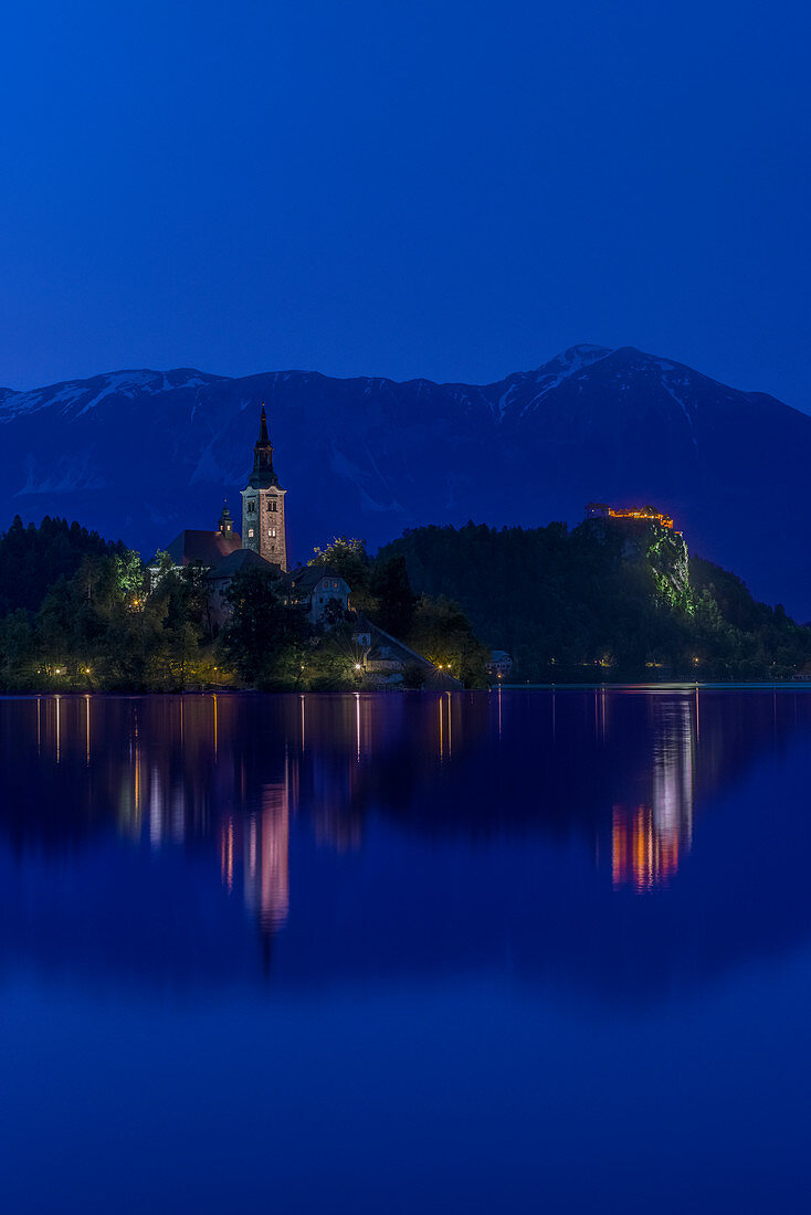 Village church and buildings reflected in still lake at night, Bled, Upper Carniola, Slovenia