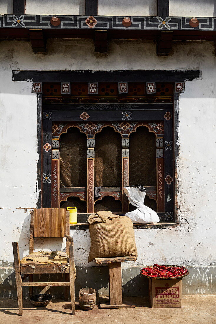 Verziertes Holzfenster, davor Stuhl und Schale mit Chili, Bhutan