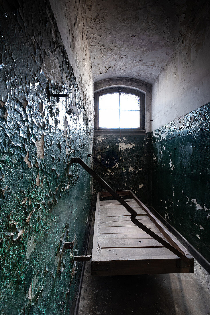 Old prison cell with original wooden platform and peeling paint on the walls, former district court prison in Berlin Köpenick, Germany