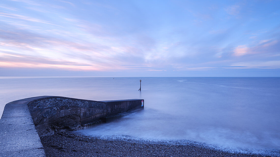 Morgendämmerung und weiches Meer hinter dem Wellenbrecher bei Sidmouth, Devon, England, Großbritannien, Europa