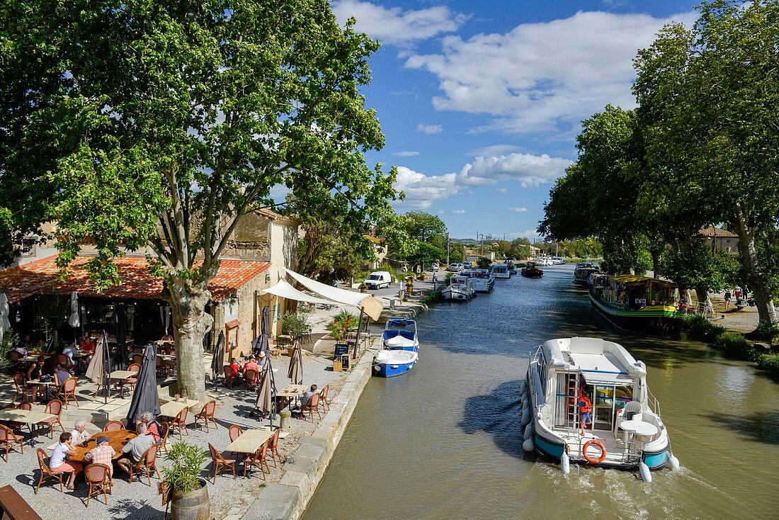 France, Aude, Saint Nazaire d'Aude, Canal du Midi listed as World Heritage by UNESCO, Port of Somail, boat of tourism passing in front of an open air dance hall in border of water