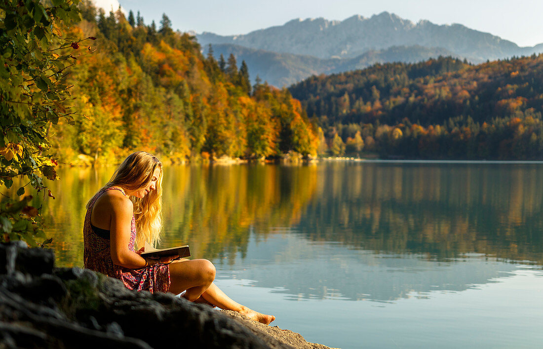 Junge Frau liest in einem Buch am herbstlichen Hechtsee, Kufstein, Tirol, Österreich