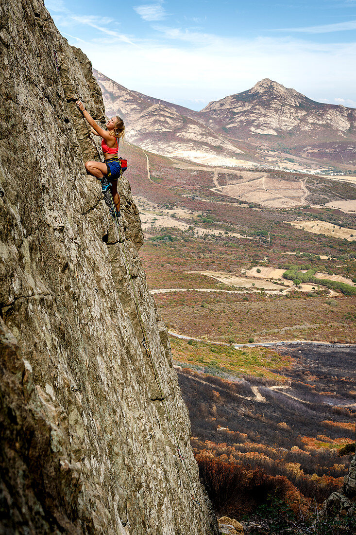 Junge Frau klettert auf plattigem Fels in Calvi, Korsika