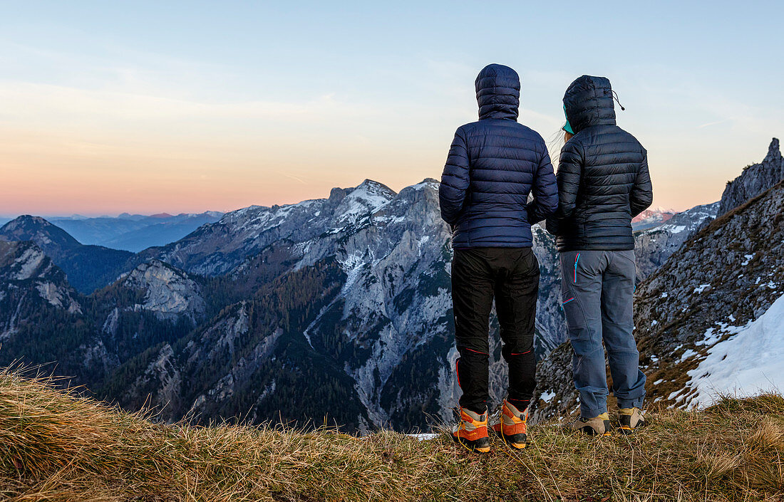 Two women in down jackets stand on the mountain and look at the Karwendel Mountains in the evening light, Gramai, Tyrol, Austria