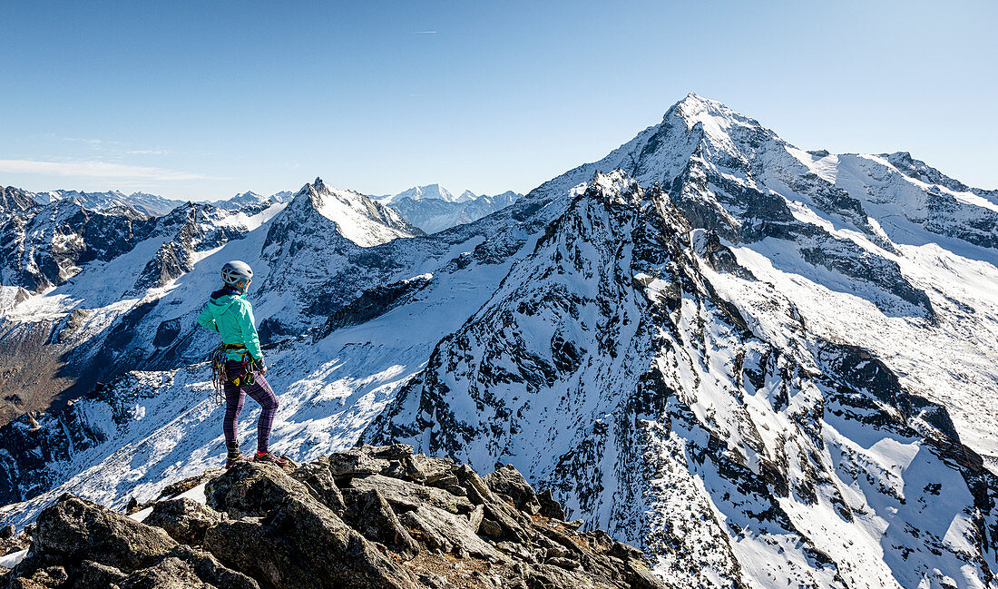 Young woman stands at the summit of the Gigalitz and looks at the high alpine landscape of the Großer Löffler, Zillertal Alps, Tyrol, Austria, which is lightly snowed in autumn